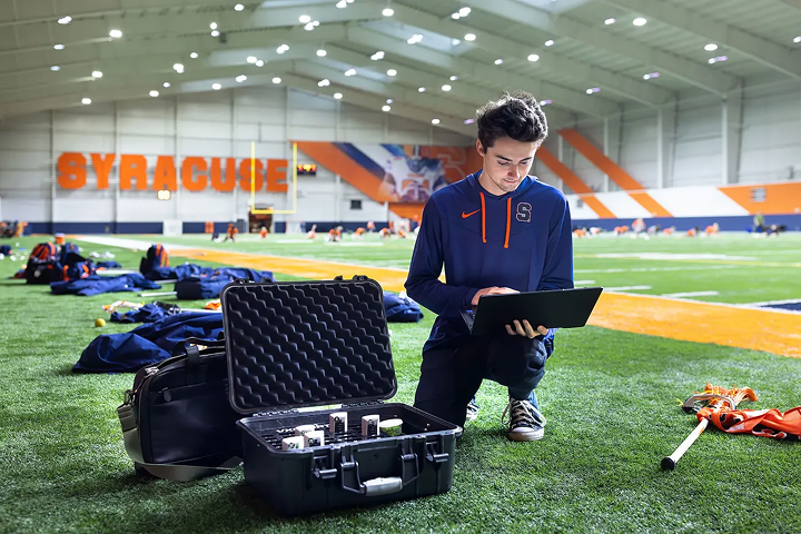 Person using a laptop on an indoor sports field.