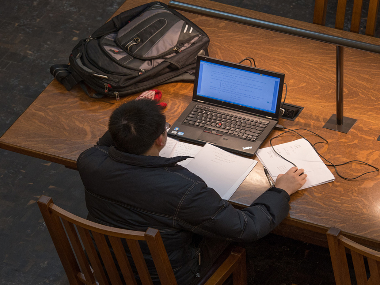 Student studying with a laptop and notes at a desk.