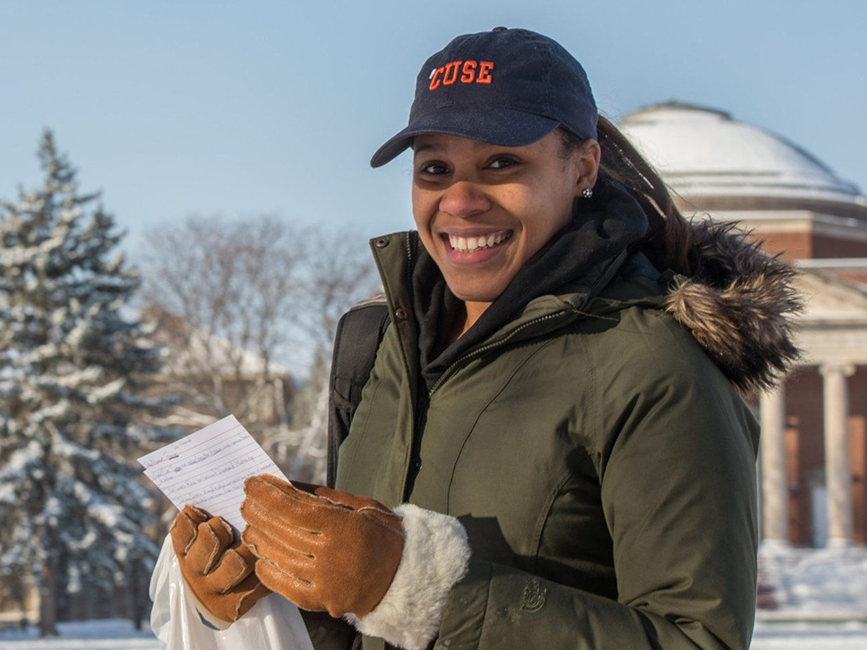 Student wearing a Syracuse cap holding a note outdoors in winter.