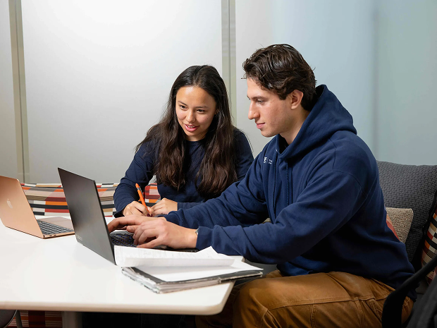 Two students collaborating on a laptop at a table.