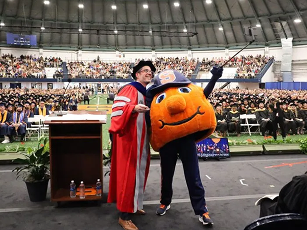 Graduate and mascot taking a selfie at a ceremony.