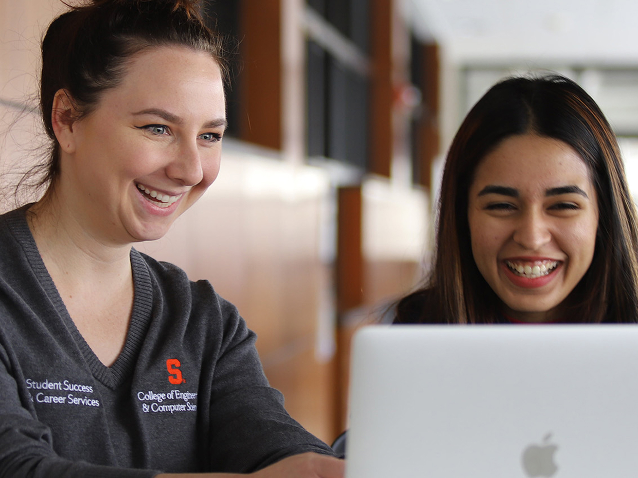 Two students smiling at a laptop.