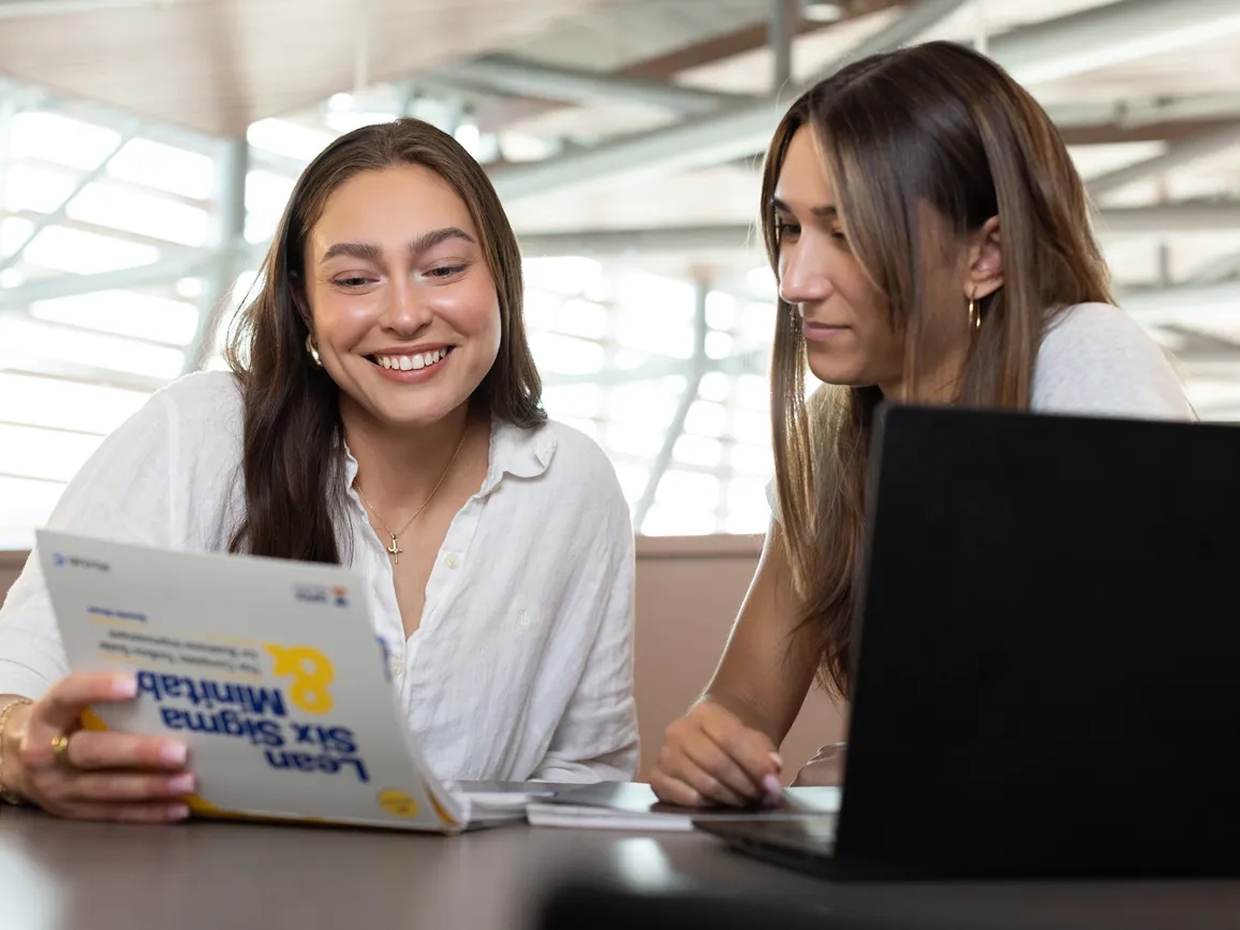 Two students reviewing materials together at a table with a laptop.
