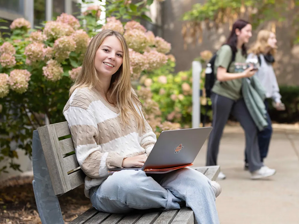 Student using a laptop on a bench.